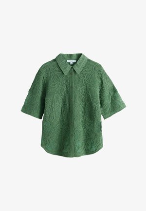 Chemise verte à manches courtes avec boutons et col, présentant un motif texturé floral et feuillu sur l’ensemble.
