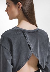 Top gris de manga larga con un diseño único en la espalda que incluye una apertura dividida, textura suave y detalle de cuello acanalado.