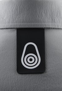 Grå tekstureret overflade med et rektangulært sort label, der har et hvidt cirkelformet design, placeret centralt.