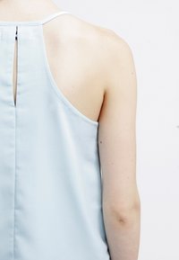 Light blue sleeveless top with a smooth texture, featuring a keyhole cutout at the back and a narrow, white shoulder strap.