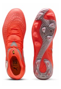 Kirkkaan oranssit jalkapallokengät, joissa on teksturoidut päälliset, nauhat ja hopeiset nastat pohjassa, esitetty ylhäältä ja alhaalta kuvattuina.