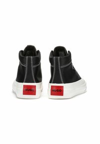 Schwarze High-Top-Sneaker mit weißen Sohlen, die kontrastierende Nähte und rote Logo-Akzente an der Ferse aufweisen. Das Material wirkt wie Canvas.