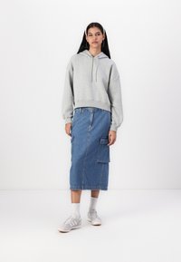 Sudadera gris corta con cordón, combinada con una falda midi de mezclilla azul con bolsillos laterales. Llevada con zapatillas blancas y calcetines ligeros.