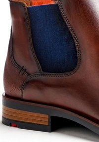 Braune Leder-Ankle-Boots mit einem blauen elastischen Einsatz, strukturierten Oberflächen, einem kontrastierenden Holzabsatz und einem kleinen roten Akzent an der Sohle.