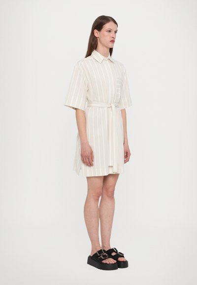 Kraeppide, lühikeste varrukatega kreemivärvi kleit, millel on peened vertikaalsed triibud. Komplekti kuulub sobiv vöö ja eesmine rinna tasku. Kanda mustade platvormkingadega.