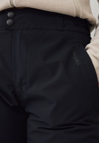 Zwart softshell broek met twee voorste knoppen, voorzien van een soepele textuur en een klein logo aan de zijkant. Geschikt voor buitensportactiviteiten.