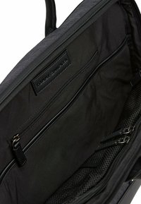 Czarna torba na laptopa z tkaninowym wnętrzem i skórzanymi akcentami. Wewnątrz znajduje się jedna kieszeń na zamek oraz siatkowe przegródki, wszystko w gładkiej teksturze.