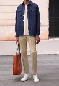Chemise bleue à boutons, pantalon beige, baskets blanches. Sac fourre-tout orange avec de légères poignées. Tissu lisse, coupe classique, deux poches poitrine.