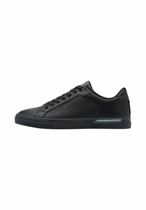 Zapatilla negra con parte superior de cuero suave y malla texturizada, puntera redonda, cordones planos negros y suela de goma con una franja de acento gris.