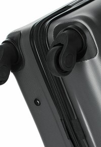 Hard-shell suitcase in textured gray material, featuring smooth black wheels, a sturdy zipper, and a black accent near the handle.