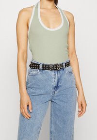 Světlý zelený halter top s žebrovanou texturou a bílým lemem, doplněný o světle modré džíny vysokého pasu a černý opasek se stříbrnými očky.