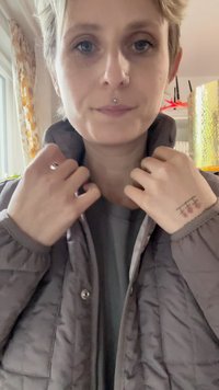 Szedá prešívaná bunda s golierom, zipsom a patentným zapínaním. Interiér je podšitý svetlejšou farbou. Ruky nadnášajú golier.
