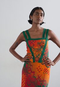 Gebreide jurk met levendige oranje, groene en rode patronen. Vierkante halslijn met brede bandjes en gestructureerde stof, aansluitend ontwerp.