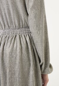 Robe en tissu texturé gris avec taille froncée et manches longues. Le matériau a un léger brillant et un motif à côtes verticales.