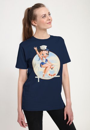 Mørkeblå t-shirt med et farverigt grafik af en tegneseriefigur i sømandsdragt, der sidder på en redningskrans med teksten "BS BOOP".