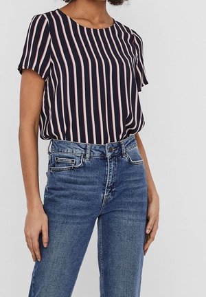 Laivastonsininen pusero, jossa on pystysuorat punavalkoiset raidat, lyhyet hihat ja pyöreä kaula-aukko, yhdistetty korkeavyötäröisiin sinisiin farkkuihin.