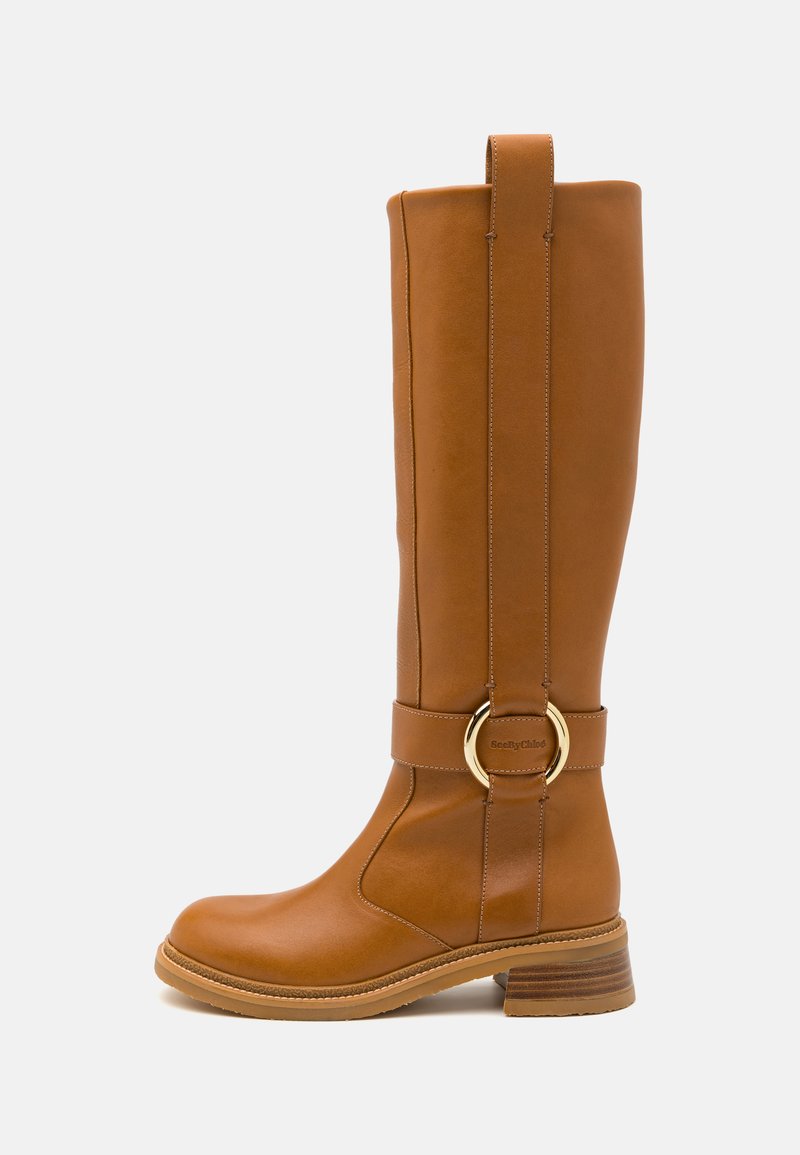 Botte en cuir marron, haute, avec un détail de boucle circulaire en or et un petit talon empilé, présentée de profil sur fond blanc.
