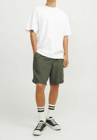 Vit, oversized T-shirt med korta ärmar, tillsammans med olivgröna shorts. Svarta sneakers, vita strumpor med svarta ränder synliga.