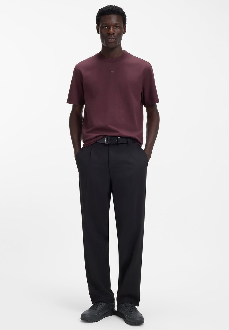 Bordeauxrotes T-Shirt mit kurzen Ärmeln und rundem Halsausschnitt, kombiniert mit schwarzen, maßgeschneiderten Hosen und abgerundet mit schwarzen Schuhen. Einfaches, elegantes Design.