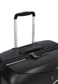 Černý pevný kufr s kovovými akcenty, teleskopickou rukojetí a kombinovaným zámkem. Má hladký povrch a elegantní design.