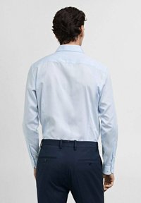 Cămașă cu dungi, albastră deschis, cu mânecă lungă și manșete cu butoni, purtată cu pantaloni închiși. Țesătură netedă, cu o croială ajustată și guler clasic.