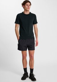 Zwarte sportieve T-shirt met korte mouwen, gecombineerd met donkere shorts. De stof lijkt glad, lichtgewicht en ademend.