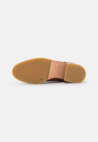 Suela de zapato de cuero marrón con una suela de goma ligera, texturizada y redonda; cuenta con un tacón de cuero cosido y el nombre de la marca en relieve.