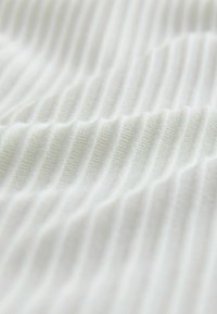 Biele žíhané tkanivo s jemným vlnitým vzorom, ukazujúce mäkkú textúru a rovnomerne rozmiestnené vertikálne rebrá po celej ploche.