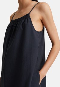 Marineblaues ärmelloses Kleid mit einem gerafften Ausschnitt, seitlichen Taschen und einer lockeren, fließenden Passform. Glatter, leichter Stoff mit subtiler Textur.