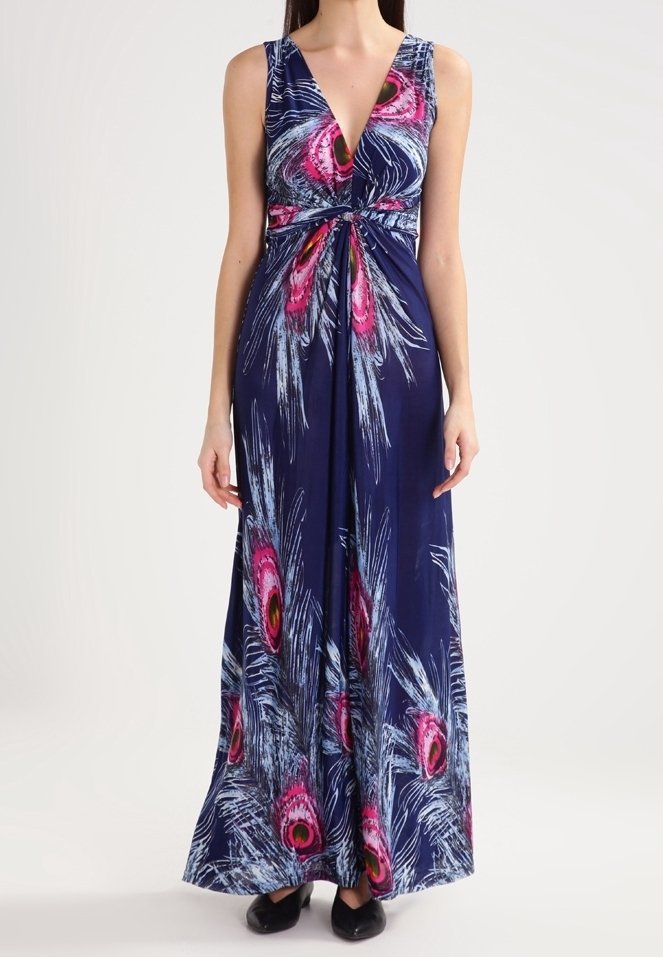 Femme portant une robe longue sans manches bleu marine avec un motif de plumes de paon rose et blanc et un décolleté en V profond.