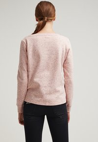 Felpa rosa chiaro con un motivo testurizzato, maniche lunghe e scollatura rotonda. Il retro presenta un design semplice e casual.