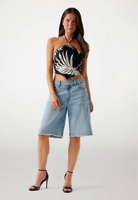 Haut dos nu noir avec imprimé feuilles de palmier blanches, associé à un short en denim bleu clair à ourlet effiloché. Sandales à talons hautes noires.