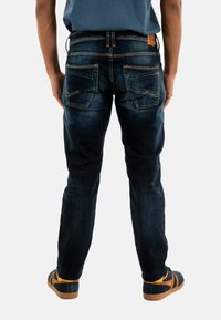 Jeans de mezclilla oscura con un diseño de pierna recta, que cuentan con tres bolsillos traseros, costuras en contraste y un parche de cuero en la cinturilla.