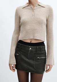 Pullover beige a coste con colletto e tre bottoni, abbinato a una mini gonna di jeans nera con tasche con zip e vita aderente.