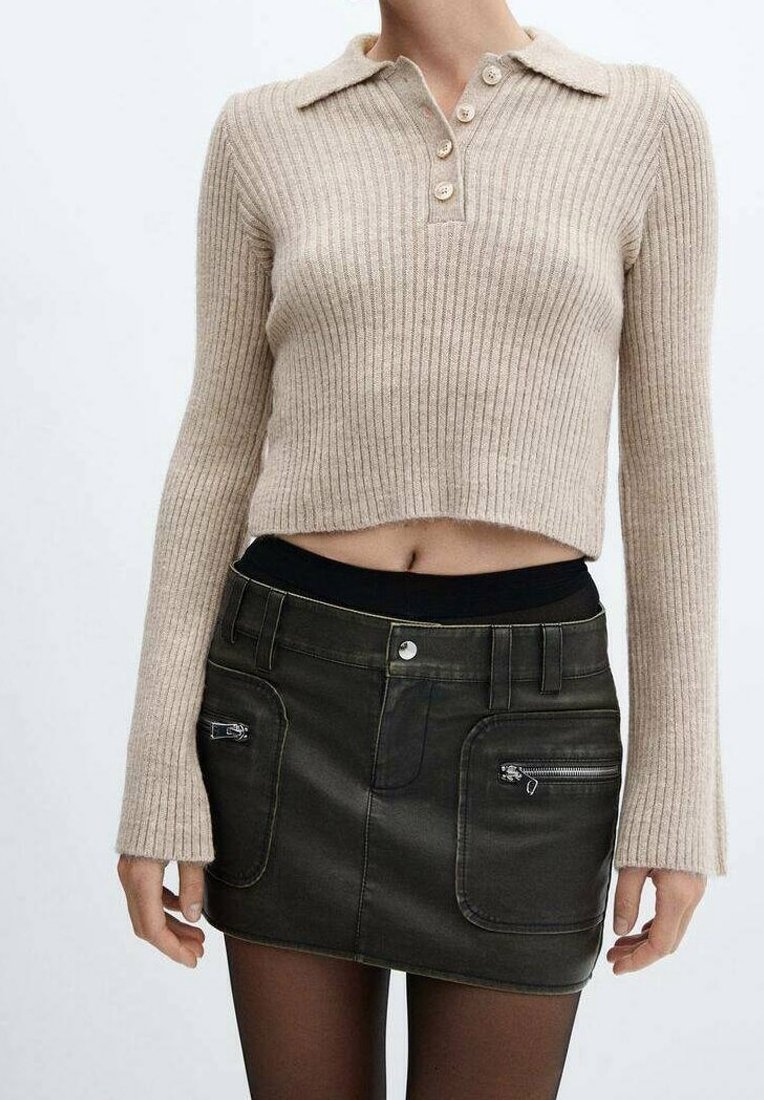 Pullover beige a coste con colletto e tre bottoni, abbinato a una mini gonna di jeans nera con tasche con zip e vita aderente.