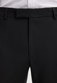 Schwarze Hose mit einer glatten Textur, flacher Front, Gürtelschlaufen und taillierter Passform. Keine sichtbaren Muster oder Akzente.