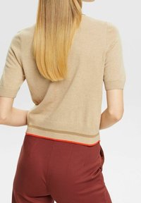 Suéter de manga corta en color beige con un dobladillo acanalado, que presenta rayas naranjas y marrones. La tela parece suave y ligera.