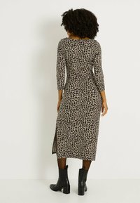 Robe midi à imprimé léopard avec manches longues, dotée d'une fente latérale et d'une silhouette ajustée. Portée avec des bottines noires.