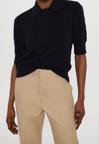 Polo blu navy con design a maglia strutturata, maniche corte e colletto. Abbinata a pantaloni beige chiaro. Bottoni sul davanti.