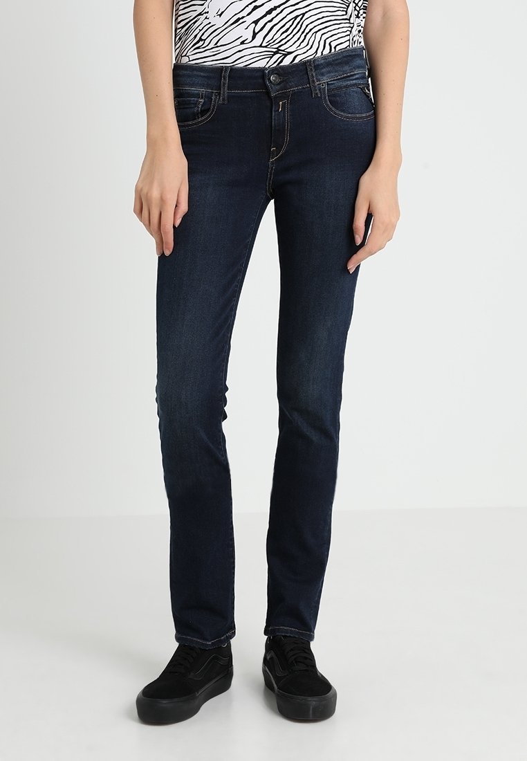 Jeans skinny blu scuro in denim, caratterizzati da un classico design a cinque tasche e una texture liscia, abbinati a sneakers nere.