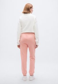 Sweatshirt branca cropped combinada com calças de treino cor-de-rosa, com punhos elásticos e um corte descontraído. A modelo usa ténis brancos.