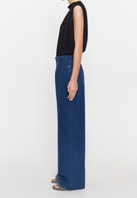 Pantalones de mezclilla azul de cintura alta con corte recto, que cuentan con cinco bolsillos y un cierre de botón. Textura suave, diseño minimalista.