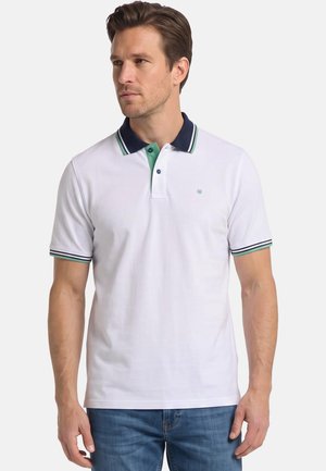 Mann trägt ein weißes kurzärmeliges Polohemd mit marineblau-grün gestreiftem Kragen und blaue Jeans, schaut leicht nach links.