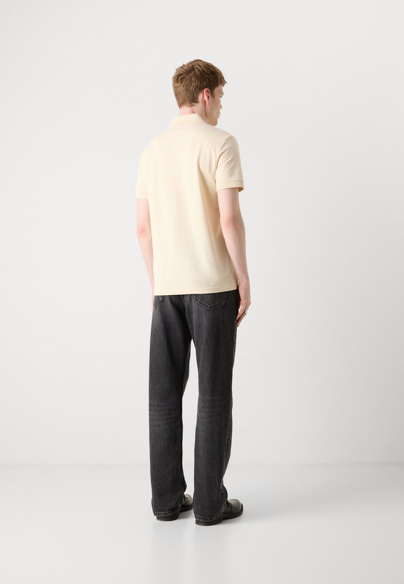 Polohemd in hellbeige, mit kurzen Ärmeln und klassischem Kragen. Kommt kombiniert mit dunkelgrauen, weiten Jeans und schwarzen Schuhen.