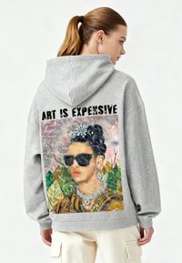 Felpa grigia con cappuccio con una grafica colorata di una donna con occhiali da sole, circondata da foglie verdi, e la scritta "L'ARTE È COSTOSA."