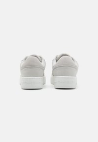 Bijele tenisice s glatkim kožnim gornjim dijelom, akcentima od suede-a na peti i gumenenim potplatom, s natpisom "TOMMY JEANS" utisnutim na peti.