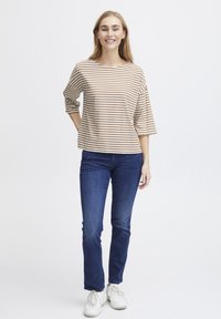 Top a righe, morbido e largo, beige e marrone con maniche 3/4, abbinato a jeans blu scuro e sneakers bianche. Design semplice e casual.