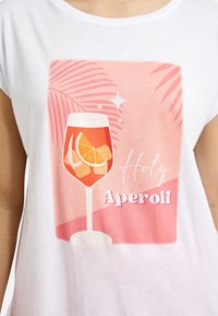 White cotton t-shirt featuring a pink graphic of a cocktail glass with ice and citrus, alongside the text "Holy Aperoli" in bold letters.