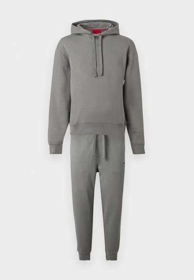 Sweat à capuche gris avec cordons, assorti à un pantalon de jogging avec une taille élastique et des poignets, sur un fond uni.