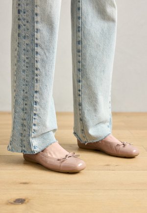 Ballerine patent rosa chiaro con dettaglio a fiocco, abbinate a jeans a vita alta blu chiaro con orli sfrangiati e una texture di denim sbiadita.